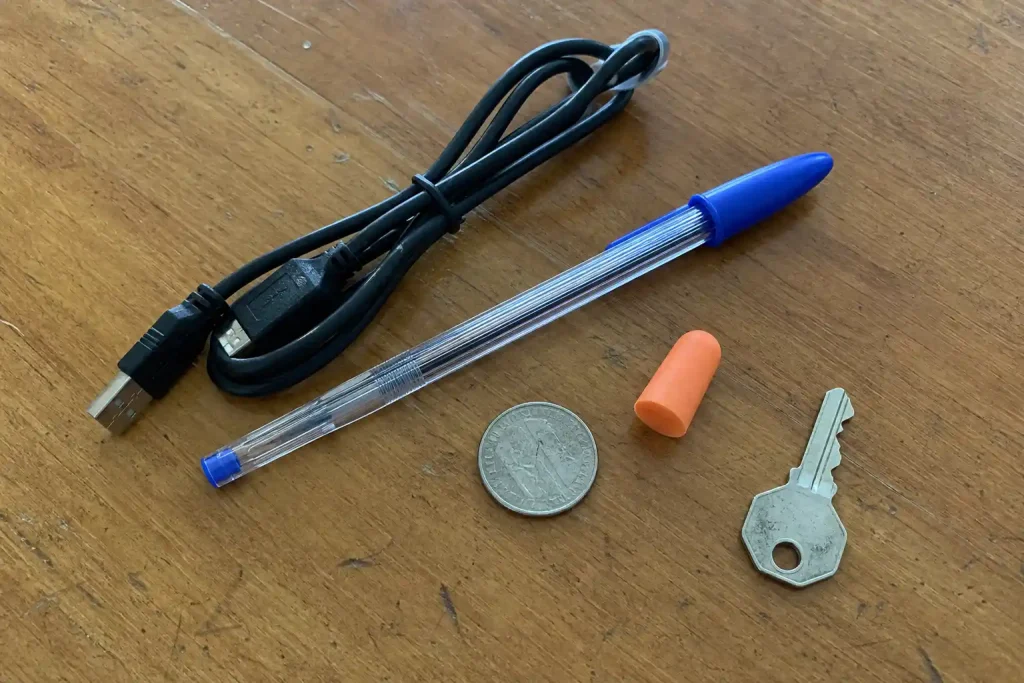 Moderna vardagsprodukter som USB-kabel, penna, mynt och nyckel ligger på ett slitet träbord.