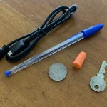Moderna vardagsprodukter som USB-kabel, penna, mynt och nyckel ligger på ett slitet träbord.